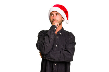 Young caucasian man celebrating Christmas wearing a santa hat isolated looking sideways with...