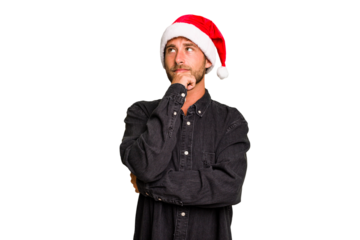 Young caucasian man celebrating Christmas wearing a santa hat isolated looking sideways with doubtful and skeptical expression.