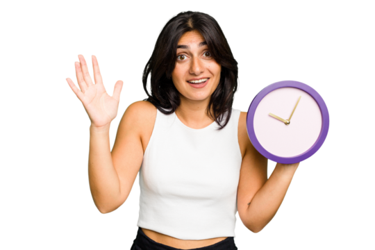 Young Indian woman holding a clock isolated receiving a pleasant surprise, excited and raising hands.