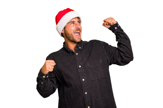 Young caucasian man celebrating Christmas wearing a santa hat isolated raising fist after a victory, winner concept.