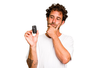 Young caucasian man holding car keys isolated looking sideways with doubtful and skeptical expression. - obrazy, fototapety, plakaty