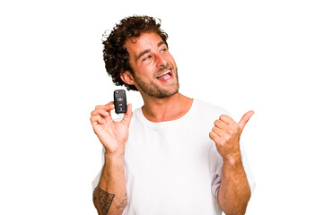 Young caucasian man holding car keys isolated points with thumb finger away, laughing and carefree.