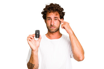 Young caucasian man holding car keys isolated showing a disappointment gesture with forefinger.