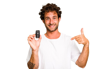 Young caucasian man holding car keys isolated person pointing by hand to a shirt copy space, proud...