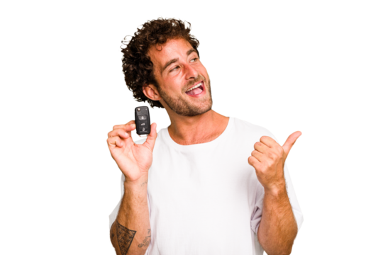 Young caucasian man holding car keys isolated points with thumb finger away, laughing and carefree.