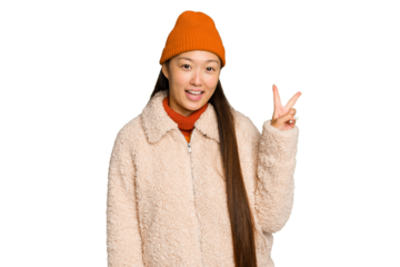 Young asian woman wearing winter clothes isolated on green chroma background joyful and carefree showing a peace symbol with fingers.