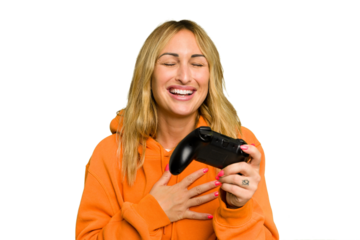 Young caucasian gamer woman holding a game controller isolated on green chroma background laughs out loudly keeping hand on chest.