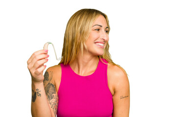 Young caucasian woman wearing hearing aid isolated on green chroma background looks aside smiling,...