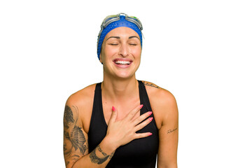 Young caucasian swimmer woman isolated on green chroma background laughs out loudly keeping hand on chest.