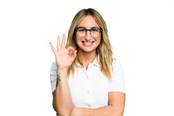 Young caucasian woman isolated on green chroma background winks an eye and holds an okay gesture with hand.