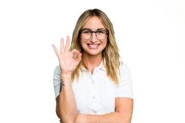 Young caucasian woman isolated on green chroma background winks an eye and holds an okay gesture with hand.