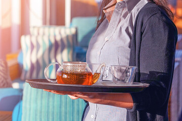 Waitress holding tray with cup of tea and tea glass teapot. Concept of maintenance and service