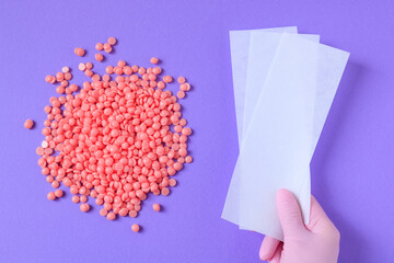 Pink granules of wax for depilation and depilatory strips on a lilac background. Epilation,...