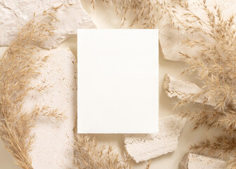 Blank card near beige travertine stones and dried pampas grass top view, greeting mockup