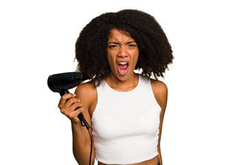 Young African American woman holding a hairdryer isolated screaming very angry and aggressive.