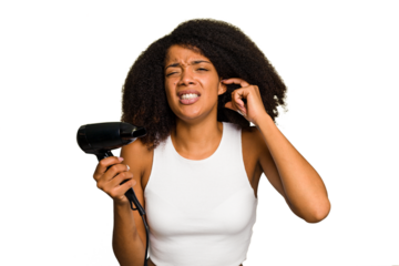 Young African American woman holding a hairdryer isolated covering ears with hands.