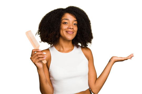 Young african american woman holding hair comb isolated showing a copy space on a palm and holding another hand on waist.