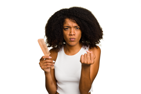 Young african american woman holding hair comb isolated showing fist to camera, aggressive facial expression.
