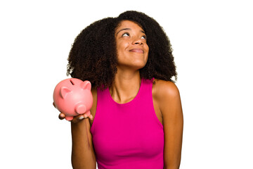Young African American woman holding a piggy bank isolated dreaming of achieving goals and purposes