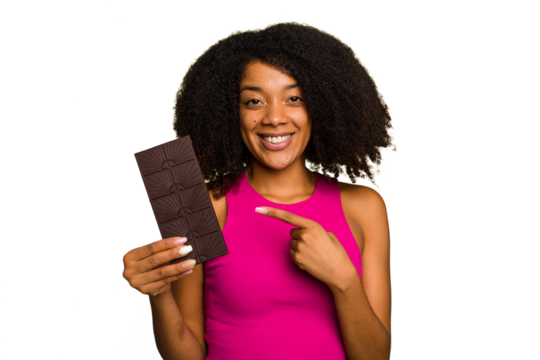 Young African American woman holding a chocolate bar isolated smiling and pointing aside, showing something at blank space.