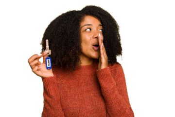 Young African american woman holding home keys isolated is saying a secret hot braking news and looking aside