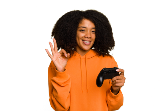 Young African American woman holding a game controller isolated cheerful and confident showing ok gesture.