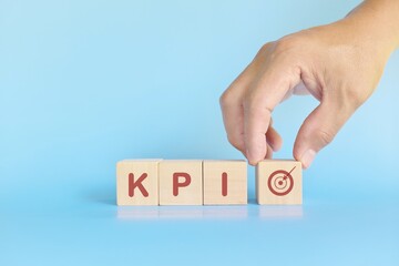 KPI or key performance indicator business target and establishment concept. Human hand stacking wooden blocks in blue background.