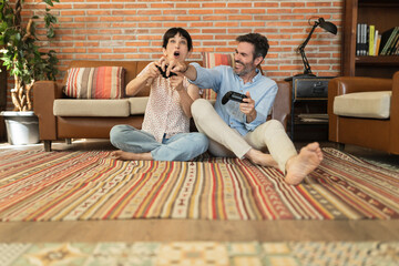 Mature couple having fun at home playing a video game with joysticks in hands. happy hispanics in...