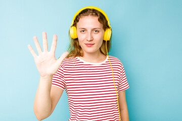 Young caucasian woman wearing headphones isolated on blue background smiling cheerful showing number five with fingers.