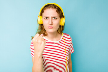 Young caucasian woman wearing headphones isolated on blue background showing fist to camera,...