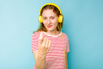 Young caucasian woman wearing headphones isolated on blue background pointing with finger at you as if inviting come closer.
