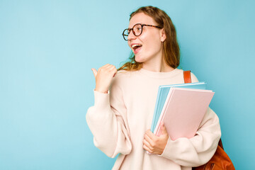 Young student caucasian woman isolated on blue background points with thumb finger away, laughing and carefree.