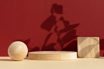 Wooden scenes of different geometric shapes on a beige table with the shadow of plant leaves on a...