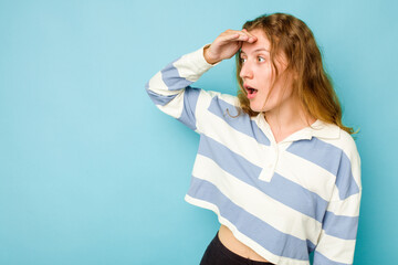 Young caucasian woman isolated on blue background looking far away keeping hand on forehead.