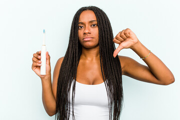 Young African American woman holding electric toothbrush isolated on blue background showing a...