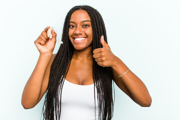 Young African American woman holding hearing aid isolated on blue background smiling and raising...