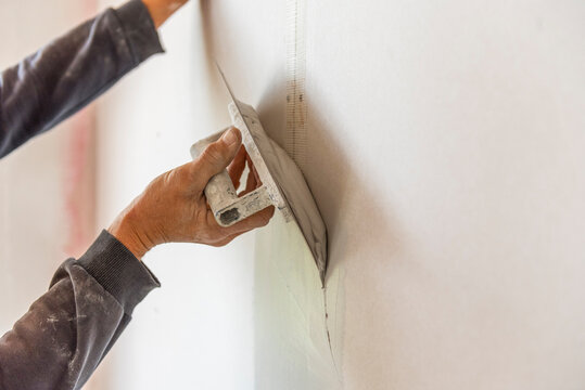 Old manual worker with wall plastering tools renovating house.