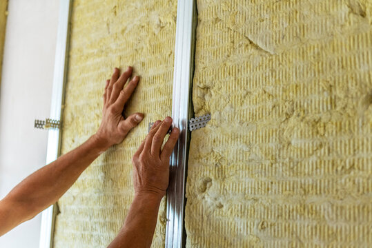 Worker insulating a room wall with mineral rock wool thermal insulation.