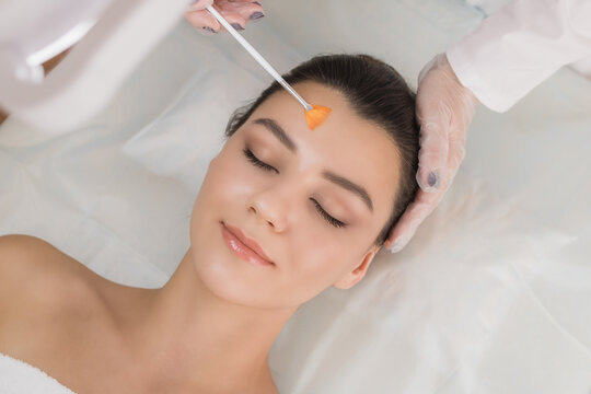 Cosmetic procedure. Chemical peeling. Doctor's hand with a brush touching the face of a young beautiful woman. Facial skin care. Place for text.