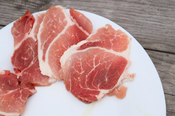 High Angle View Of Slised Meat In White Plate On Table. Fresh steak in plate. Uncooked raw pork meat slices on a white plate and wooden table.