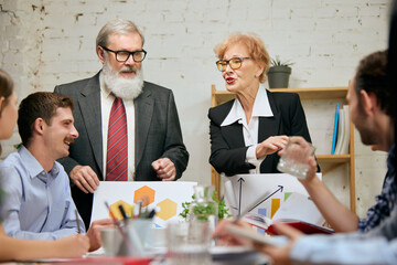 Friendly atmosphere at business gathering. Mixed ages people talking, working with colleagues at loft style office space, indoors.