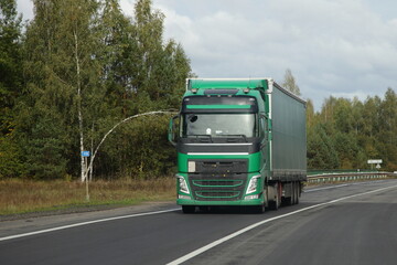 Fototapeta na wymiar Green semi truck drive on countryside highway road front view. Goods import in Europe
