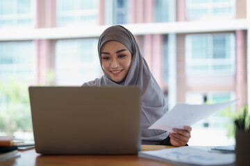 eautiful Muslim woman using computer and documents working in office