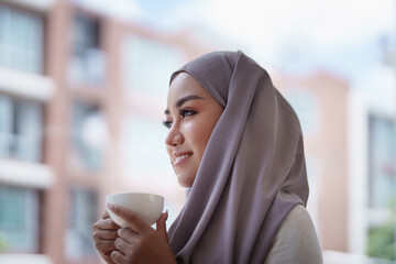 A beautiful Muslim woman with a smiling face in the morning drinking coffee and using a computer