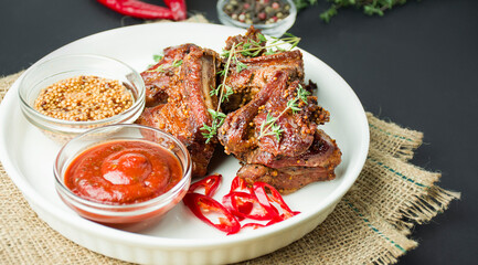Baked ribs on a white dish. Grilled pork ribs with spices and herbs on a dark background. Food...