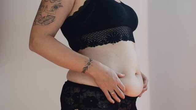 Tattooed woman in black underwear with fat belly, overweight female body isolated on white background. Lose weight. concept of surgery, subcutaneous fat breakdown.