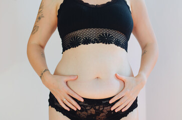Tattooed woman in black underwear with fat belly, overweight female body isolated on white background. Lose weight. concept of surgery, subcutaneous fat breakdown.
