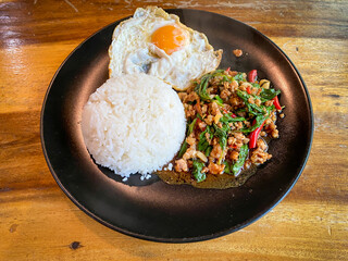 Rice topped with stir-fried pork and basil with a fried egg on the table