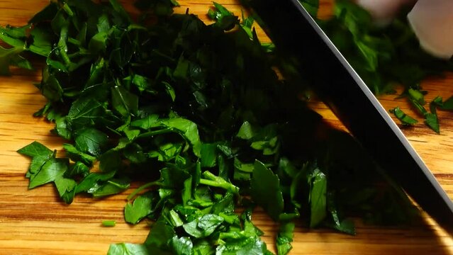 Chef chopping parsley leaves with a knife on a cutting