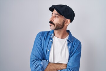 Hispanic man with beard standing over isolated background looking to the side with arms crossed convinced and confident